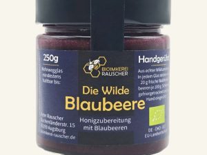 Vorderansicht des 250g-Glases „Die Wilde Blaubeere“ der BioImkerei Rauscher mit dunkelblauem Etikett und cremigem Blaubeer-Honigaufstrich.
